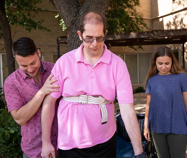 Male physical therapist working with male patient outside female visitor is providing support in the courtyard of Moody Neuro Institute