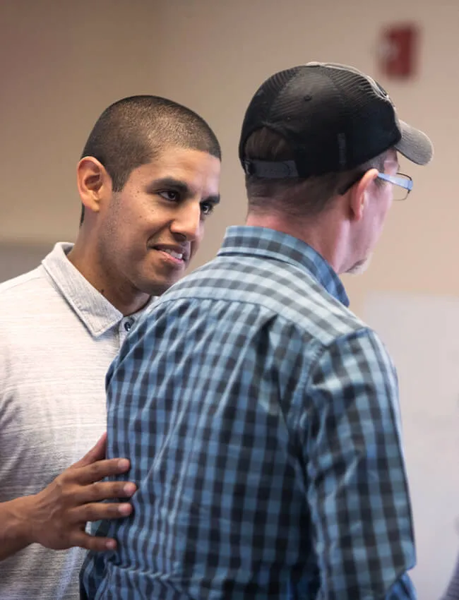 Male patient admissions rep walking male patient in blue plaid shirt and black and grey baseball hat down the hallway at Moody Neuro Institute