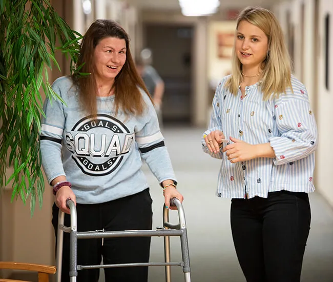 Female patient admissions rep walking female patient on walker down the hallway at Moody Neuro Institute