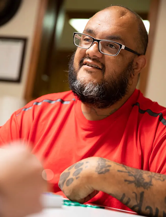 Male patient in red shirt and glasses smiling during a friendly game of Scrabble during recreational therapy at Moody Neuro Institute