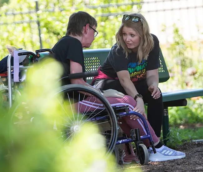 Female patient in wheelchair outside having a conversation with another female at Moody Neuro Institute